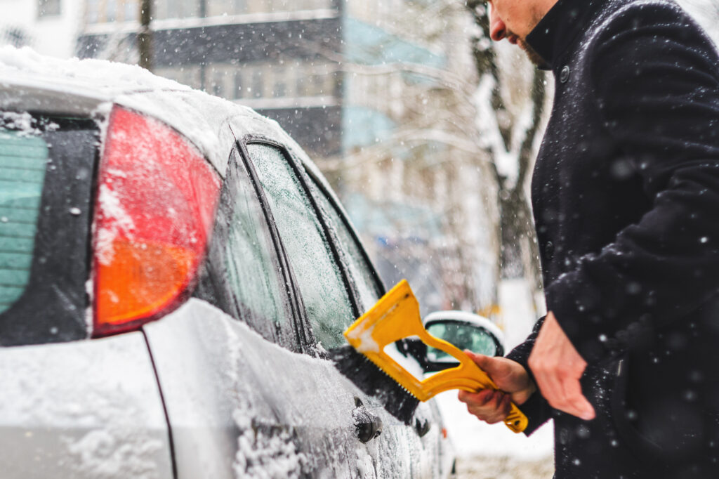 車に積もった雪をブラシで落としている様子