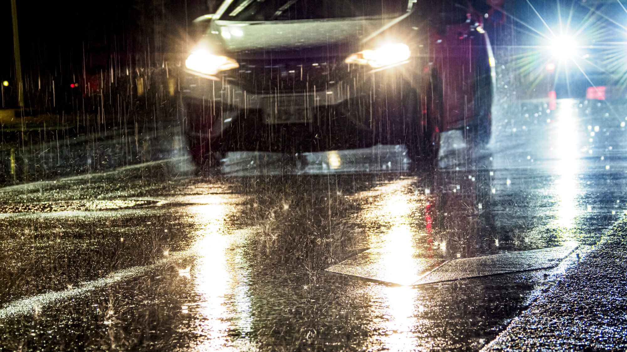 雨にヘッドライトオンで走る車