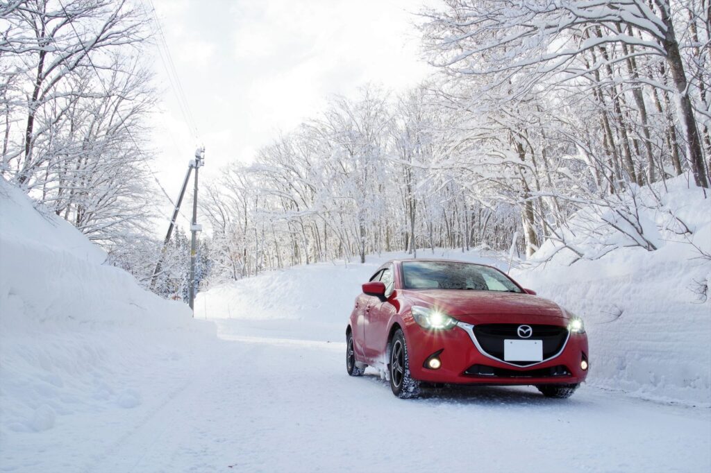 雪の中、フォグランプを点灯して走行する赤い車