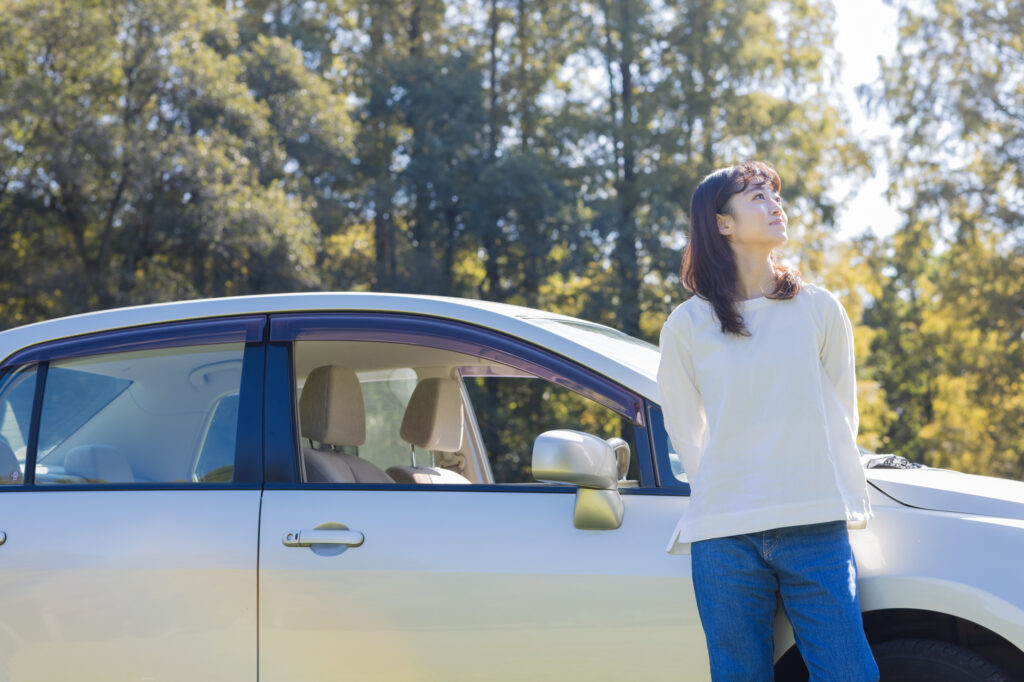 木々のそばに車を停めて休む女性