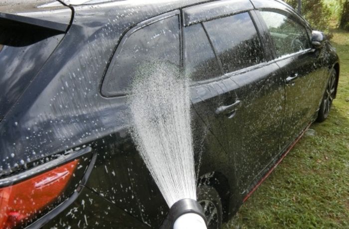 手洗い洗車の泡をホースの水ですすいでいる様子