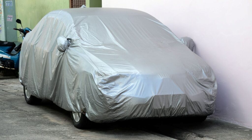車が雨に濡れるのを防ぐためにボディカバーを付けている様子